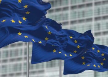 group of flags of the European Union waving in the wind in front of the European Parliament building. Seamless loop in slow motion. Selective focus